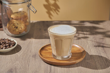 hot creamy milk in coffee is served with cookies. hot latte coffee drink in glass with cream milk on wooden table.  breakfast beverage morning concept.