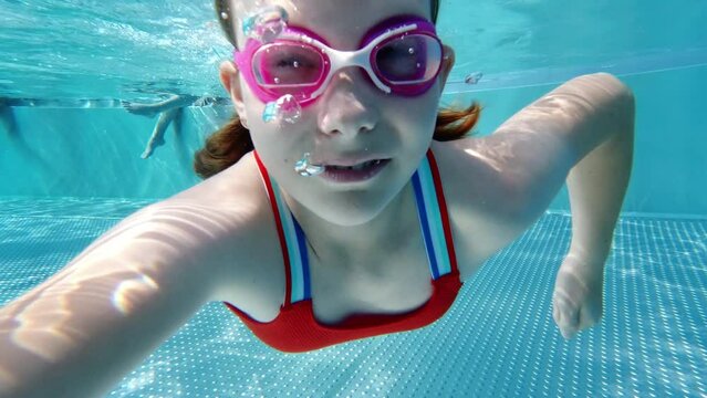 Slow motion video of diving little girl making bubbles underwater in swimming pool