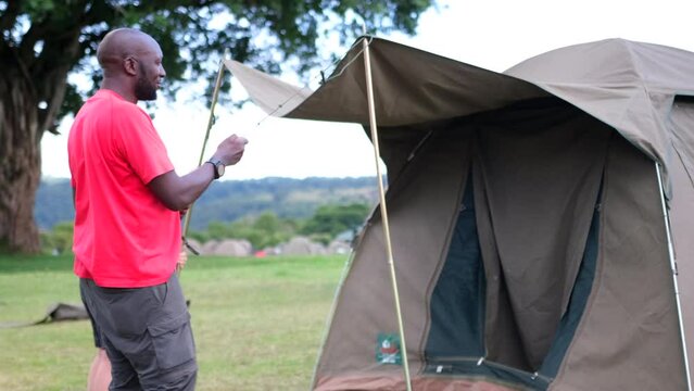 A black man with his white assistant sets up a tent for tourists to spend the night at a Seronera campsite in the Serengeti National Park, Tanzania, Africa