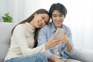 Happy couple love at home,beautiful two asian young spending good time together,bonding to each other and smiling romantic on sofa in living room while man embrace woman using smartphone, mobile phone