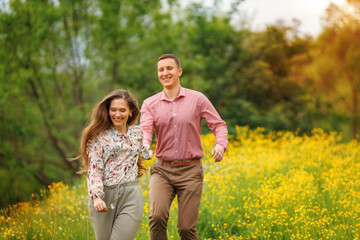  Happy loving couple are running together and holding hands, two people enjoying a walk through grass land. The young woman laughs and her hair flutters