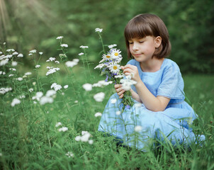 süßes kleines Mädchen in einem blauen Kleid mit einem Strauß Gänseblümchen sitzt auf einer Blumenwiese im Park