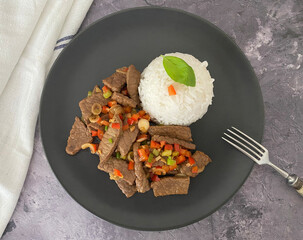 Stir fry, marinated, fried strips of beef with chili pepper, basil and spring onions, served with rice.