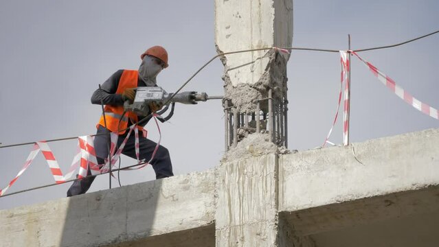 A builder worker in a mask works with a jackhammer at a construction site.