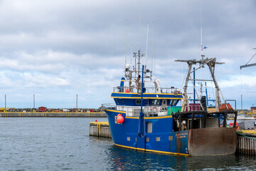 A blue fishing boat sits idle in Bonavista Harbour, Newfoundland, on a gloomy and overcast day.