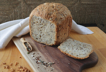 loaf of homemade whole grain bread and a cut slice of bread on a wooden cutting board. Mixture of seeds and whole grains. Healthy eating