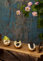 Wooden tray with bread rolls, three have vegan cream or cheese spreads, black olives and seeds, cheese, lettuce,  photo vertically
