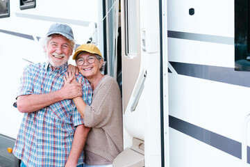Cheerful senior couple on leisure trip standing outside a camper hugging each other and looking at...