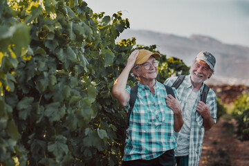 Senior couple of tourists in Tenerife travel visiting vineyard walking amongst grapevines. People on holiday wine tasting experience in summer valley landscape.