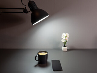 A table lamp illuminates a cup of coffee and a phone.