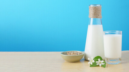 Milk bottle and milk glass with cookie and white flower on wood. Blue background.