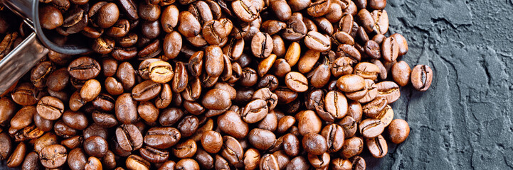 Roasted coffee beans in metal cup on a black background.Copy space. Banner