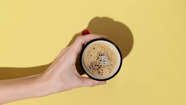 Woman hand holding a cup of coffee on yellow background. Minimalist style. Stop motion animation.