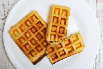 Freshly cooked Belgian waffles on a white plate on a light wooden background.