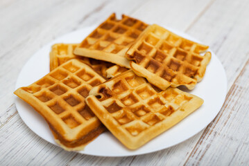 Freshly cooked Belgian waffles on a white plate on a light wooden background.