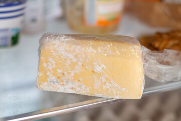 Moldy cheese wrapped in cling film in the refrigerator. Incorrect storage, spoiled product, expired...