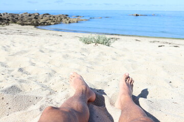feet on the sand with the sea in the background
