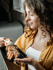 A girl in an orange shirt, white top and blue jeans holds sushi with chopsticks © Oleksandr Rudenko