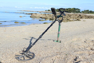 Metal detector at the beach on the sand with a green shovel with the sea in the background