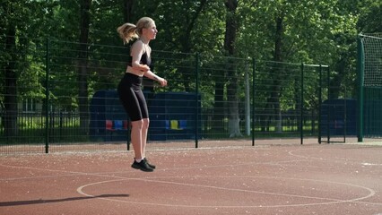 Young woman doing jump rope exercises outdoors. Athlete female doing jump exercise before running. Sporty girl doing cardio exercise with jump rope. Full length in 4K, UHD