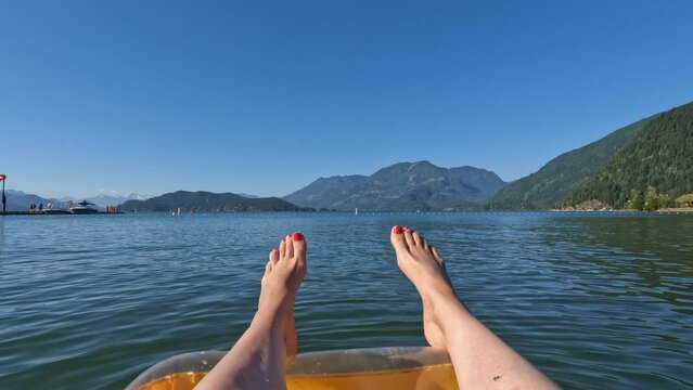 Close up view of a female legs hanging down from a lilo while floating on the beautiful Harrison Lake surrounded with mountains in Harrison Hot Springs