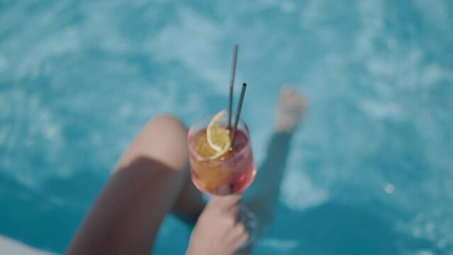 cocktail in the hands of a woman by the pool. The feet float in the pool water. Selective focus. basin.