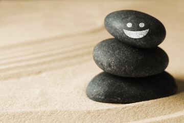 Fototapeta na wymiar Stack of stones with drawn happy face on sand, space for text. Be in harmony and enjoying your life