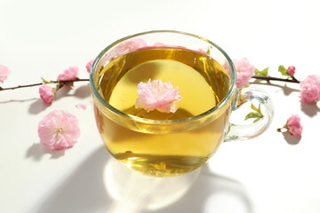 Glass cup of freshly brewed tea and beautiful flowers on light table