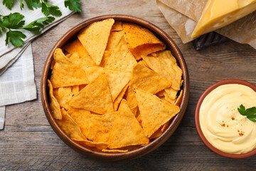 Delicious nachos and cheese sauce with parsley on wooden table, flat lay