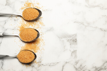 Spoons with brown sugar on white marble table, flat lay. Space for text