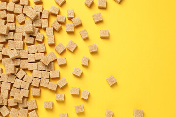 Fototapeta na wymiar Brown sugar cubes on yellow background, flat lay. Space for text