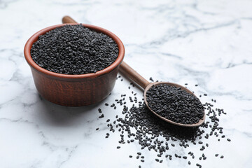 Bowl and spoon with black sesame seeds on white marble table