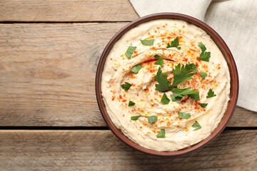 Tasty hummus with parsley and paprika in bowl on wooden table, top view. Space for text