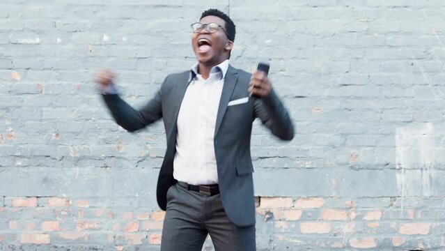 Celebrating business man cheering his promotion, success or achievement after reading a message on his phone while outside in the city. Cheerful young corporate professional overjoyed with good news