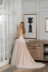 The beautiful woman posing in a wedding dress. Young beautiful happy bride wearing white wedding dress and posing in bright empty interior. Wedding fashion. Expensive Lace bust.