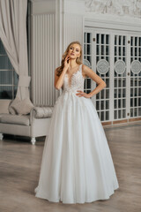 The beautiful woman posing in a wedding dress. Young beautiful happy bride wearing white wedding dress and posing in bright empty interior. Wedding fashion. Expensive Lace bust.