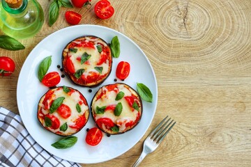 Mini eggplant pizzas-eggplants with pizza sauce,mozzarella cheeses,tomatoes,olive oil,basil,salt and peppers on plate with wooden background.Healthy summer vegetarian food.Top view.Copy space
