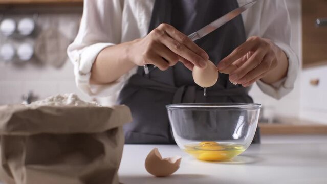 Whisking eggs cooking homemade food, Cook in the kitchen breaks colitis egg shell, Whisking eggs to make pastry dough, Egg yolk falls into a glass bowl bowl
