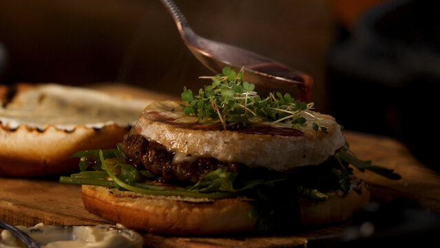 Male chef preparing burger at the restaurant kitchen. Stock footage. Close up of male hands adding wine and cranberry sauce to the tasty delicious beef burger, foodporn. - Powered by Adobe