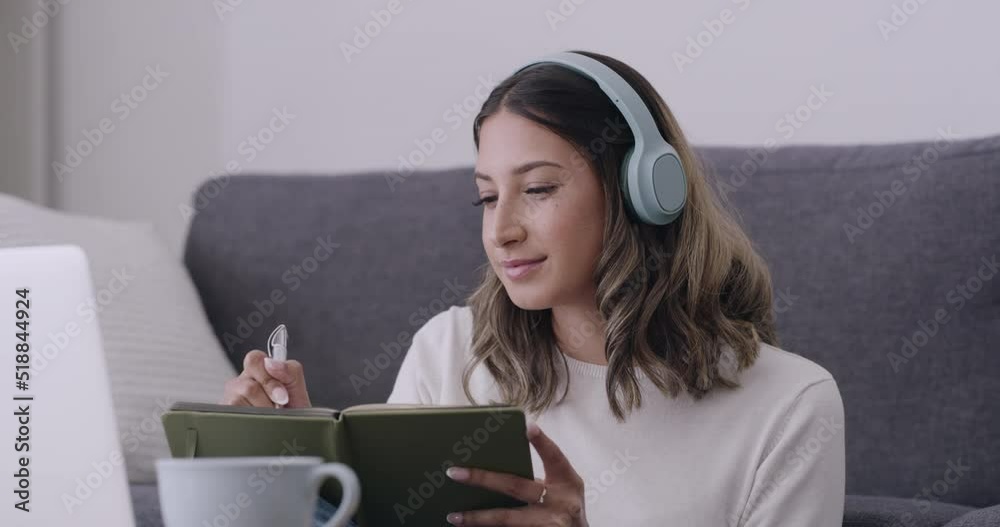 Poster student studying online course classes at home writing down notes in her note book while wearing wir