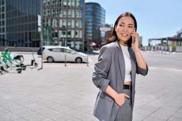 Young happy Asian successful businesswoman entrepreneur wearing suit standing in big city talking...