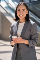 Smiling confident successful young 30s Asian businesswoman wearing suit standing on urban street...
