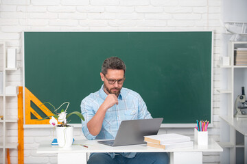 Portrait of mature teacher or tutor professor working at table in college or high school. Education and knowledge concept.