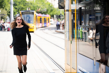 Beautiful woman in fashionable summer spring clothes outdoors running after trolleybus bus and pulling trolley case. Female model walking city street. Summer trend, fashion outfit. Traveling in city.