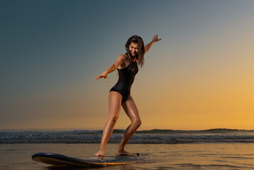 Fototapeta na wymiar Surfing training. Surf lessons. Girl with surf board ready to surfing. Woman surfer on the surfboard on a beach at sunset.