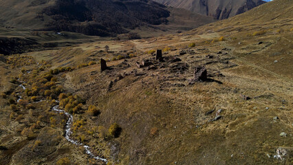 Fototapeta na wymiar Old cemetery with ruins of ancient tombs located in mountains. Footage. Aerial view of the ancient burial place with brick wrecks on the background of mountain slope covered by trees.