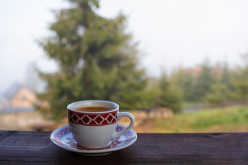 cup of goffee on wooden table. green pine tree in the background.