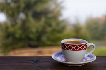cup of goffee on wooden table. green pine tree in the background.