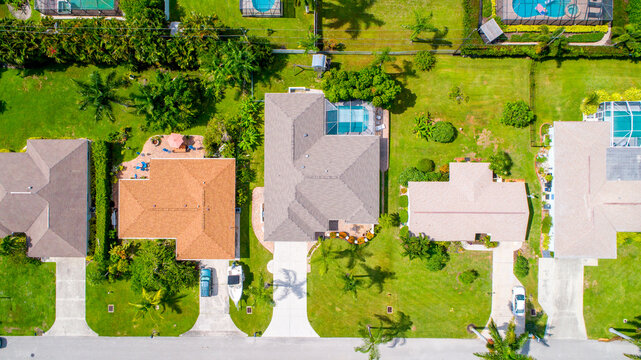 Aerial Drone Perspective Looking Down on Home Roofs with Beautifully Landscaped Real Estate and Palm Trees on a Street in Florida 