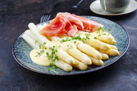 Modern Style traditioneller ged&auml;mpfter wei&szlig;er Spargel mit Rohschinken und Sauce Hollandaise serviert als close-up auf einem Nordic Design Teller